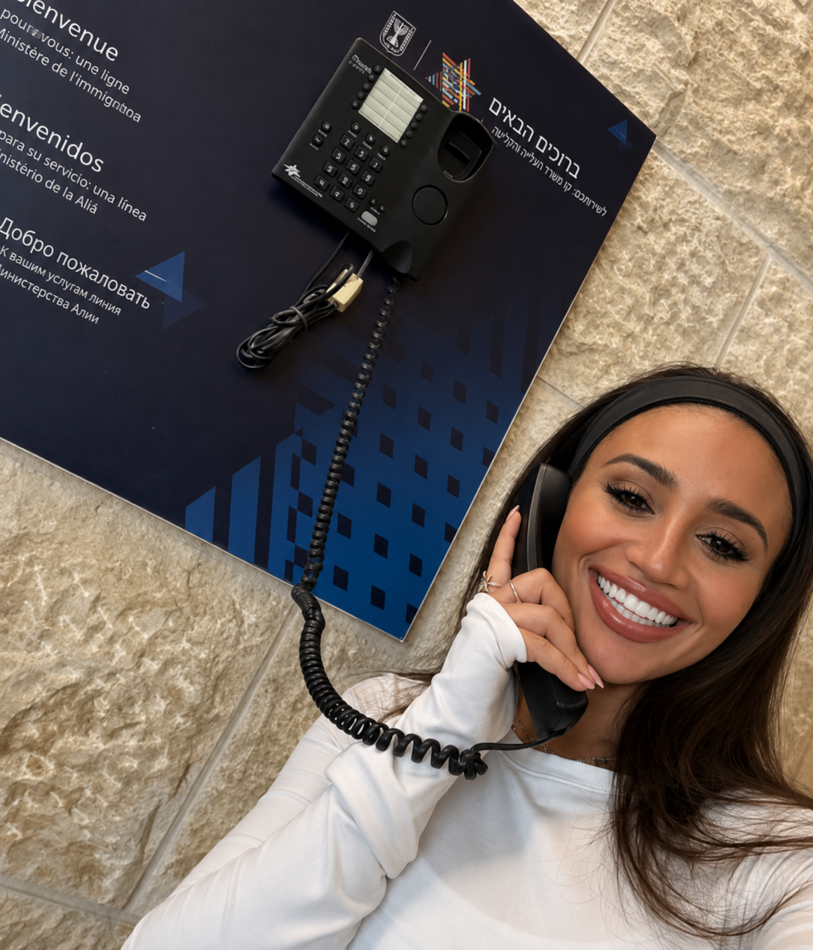 A woman smiling while using the immigration ministry welcome phone after making Aliyah