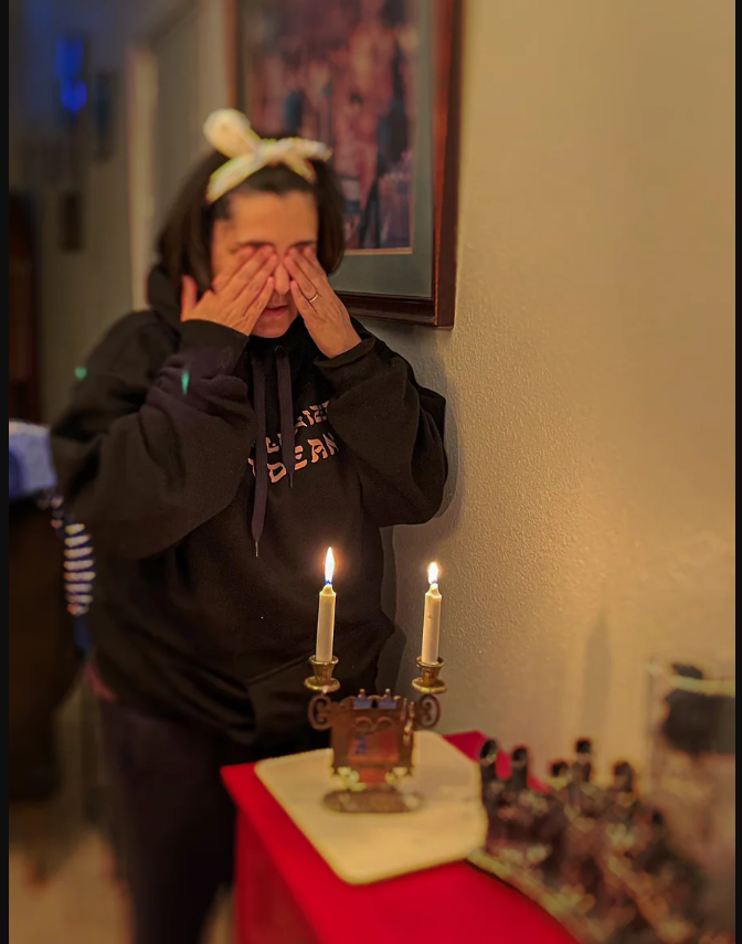 Yasmine lighting candles in a Decolonized Judean hoodie